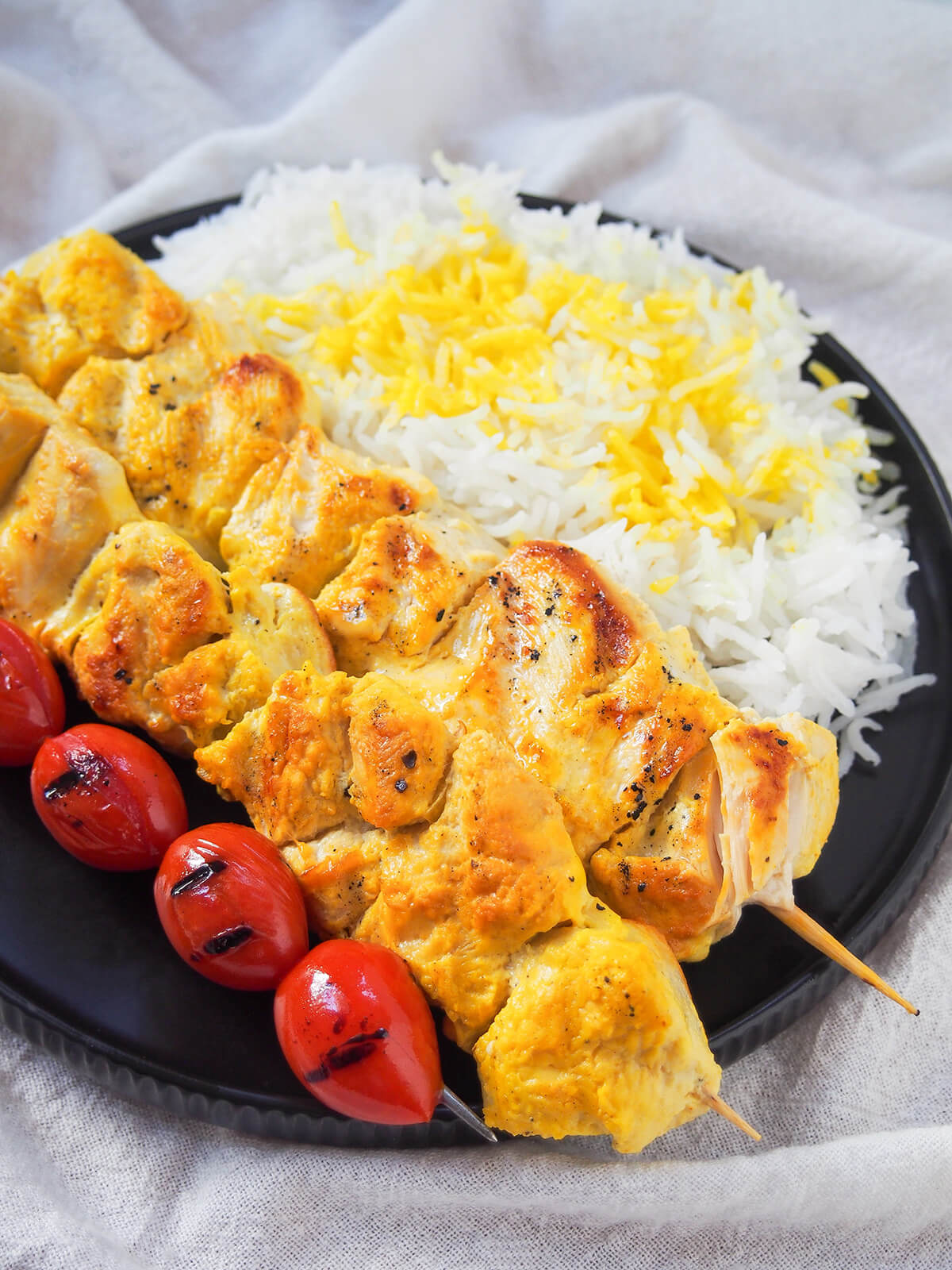 partial side view of jujeh kabab, tomatoes and rice on plate.