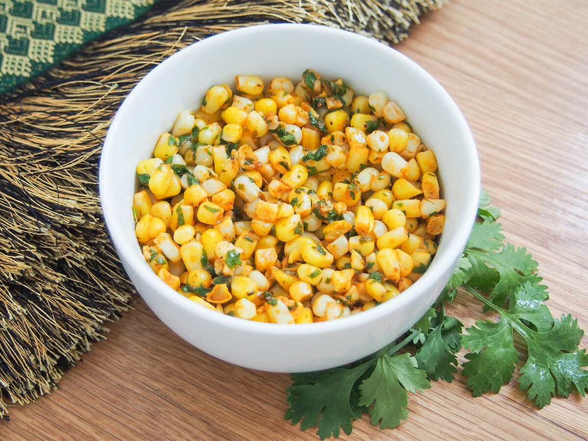 side view of bowl of masala corn with stem of cilantro below bowl.