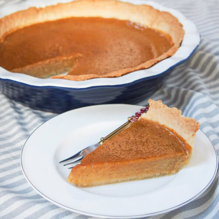 slice of pumpkin pie on white plate in front of rest of pie in pie dish.