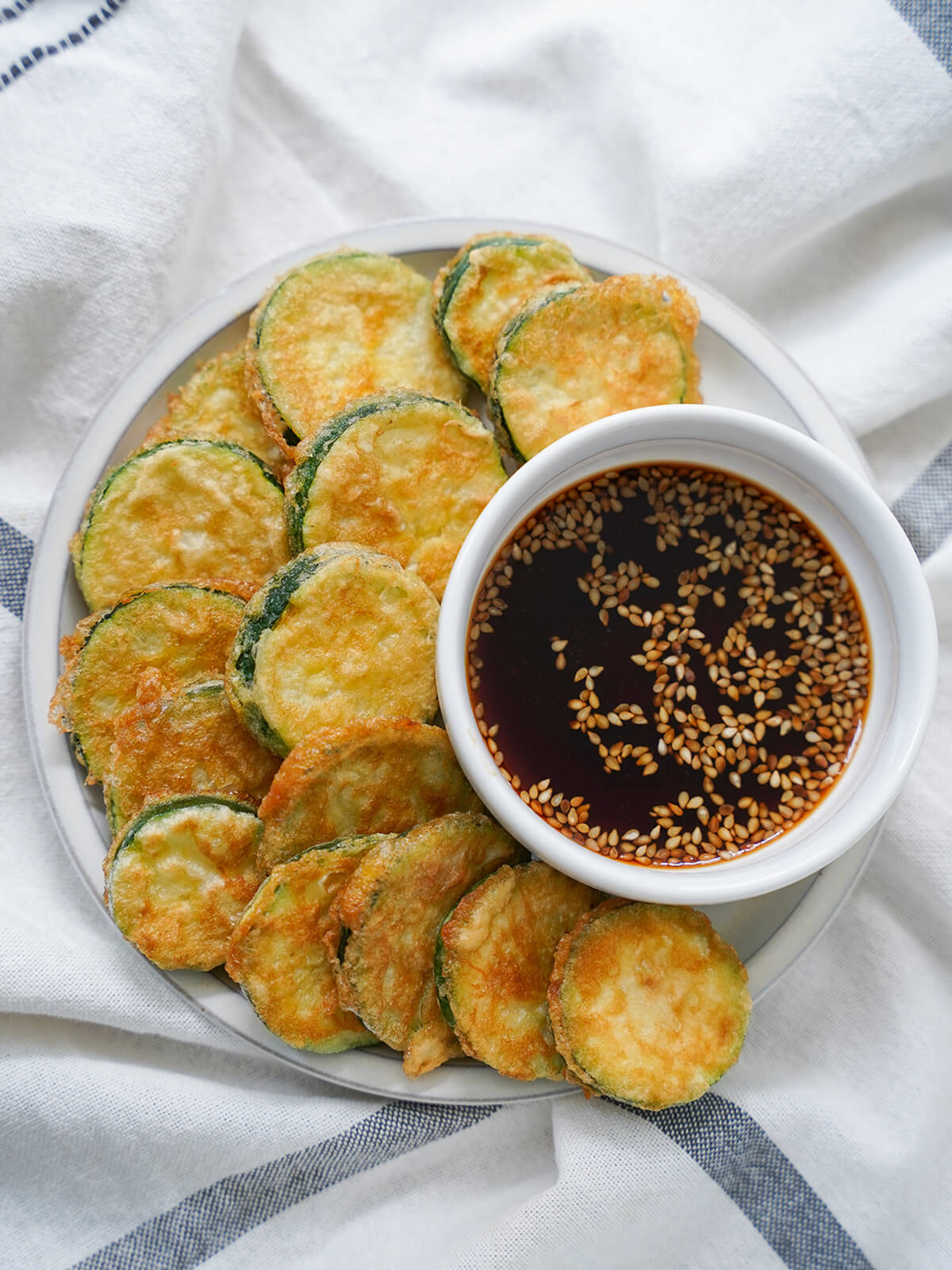 overhead view of plate of Korean zucchini fritters, hobak jeon with dipping sauce ot one side.