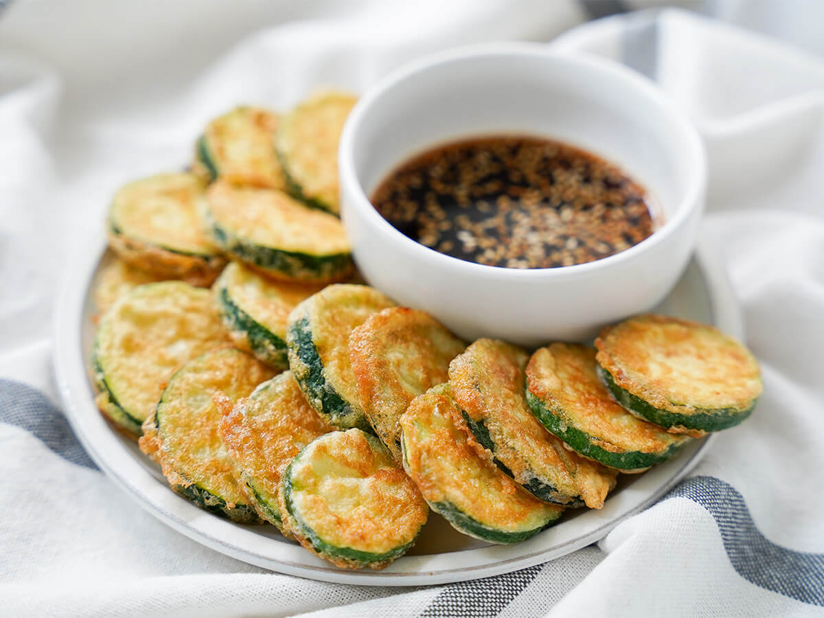 plate of Korean zucchini fritters, hobak jeon with dipping sauce to back.
