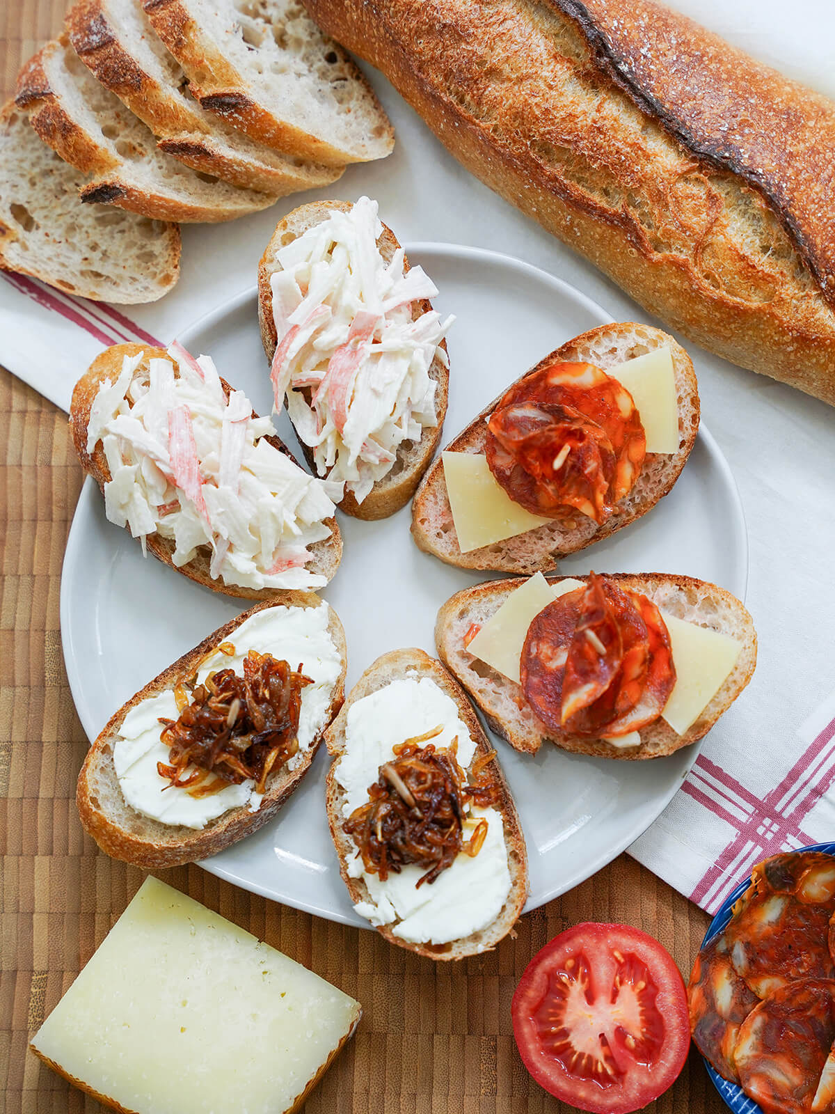 Spanish pintxos are simple finger food tapas that have lots of scope for variety. Get some inspiration, try some easy pintxos recipes and enjoy these tasty bites at home. plate showing three different Spanish pintxos recipes with bread above plate and cheese, tomato and chorizo below.