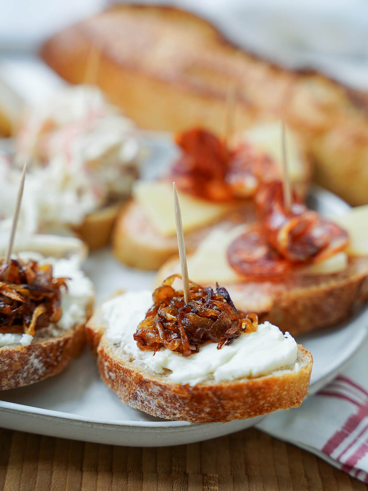 close up of goat cheese and caramelized onion pintxo with others behind side view of some classic Spanish pintxos with goat cheese and caramelized onion ones towards front.