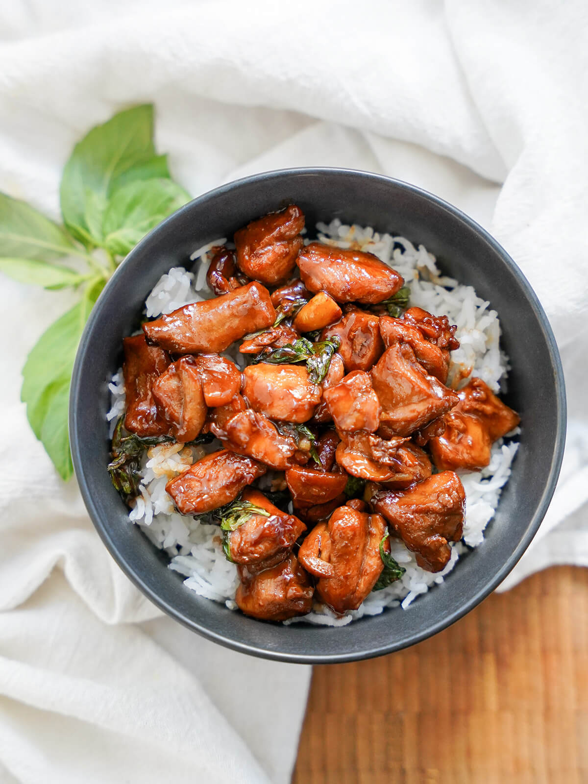 Taiwanese three cup chicken makes a delicious, easy and comforting meal. overhead view of a bowl of Taiwanese three cup chicken with Thai basil leaves below bowl.
