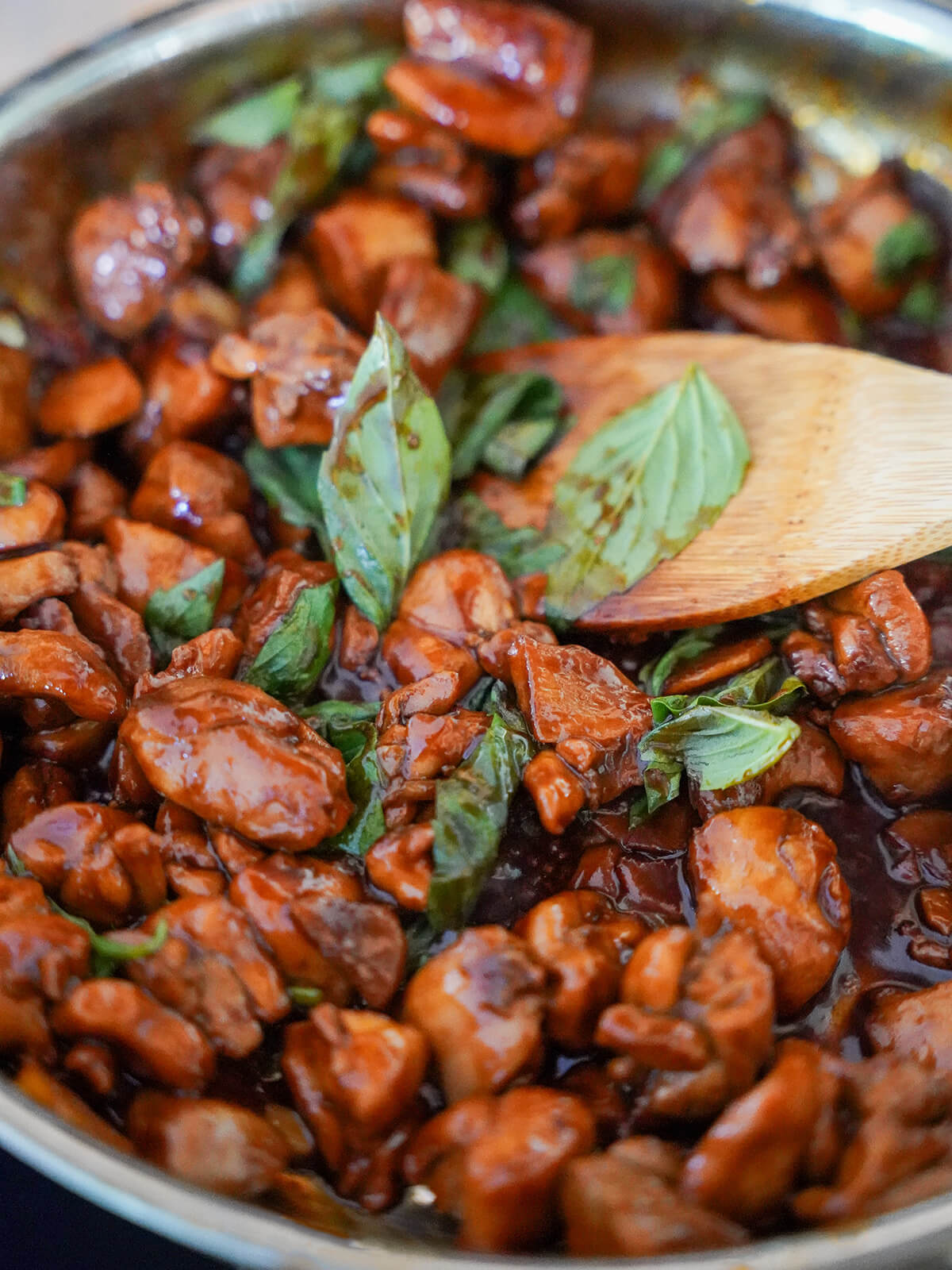 stirring Thai basil leavesinto skillet of Taiwanese three cup chicken.