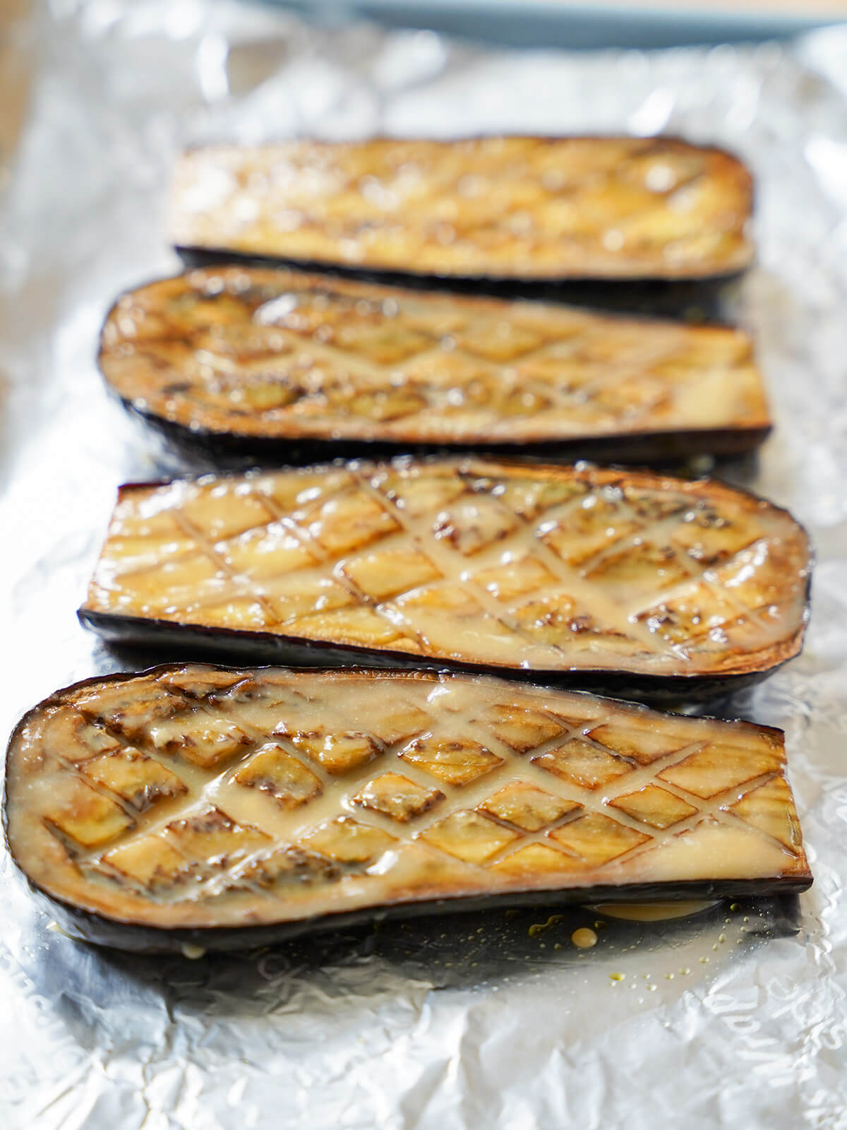 hatch-patterned topped eggplant with miso glazo ver the top of them on foil.