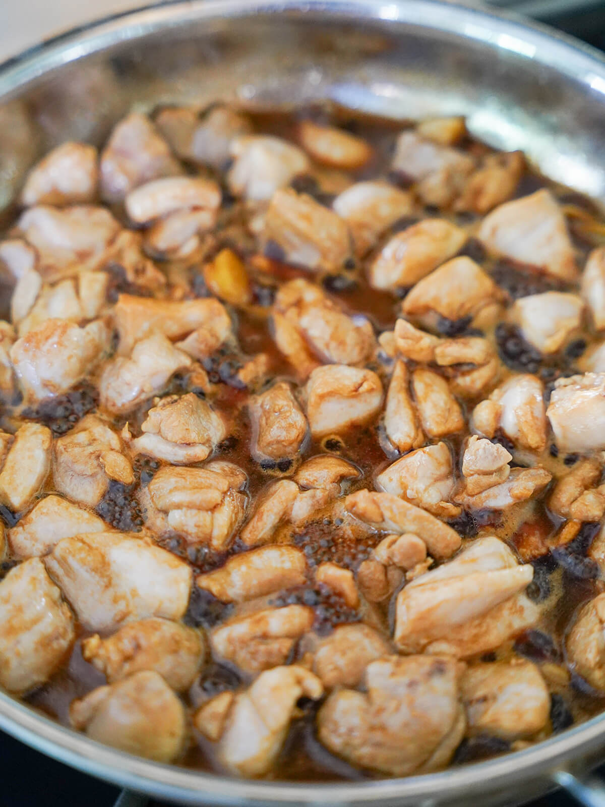 add sauce to chicken for Taiwanese three cup chicken sauce around chicken starting to simmer in skillet.