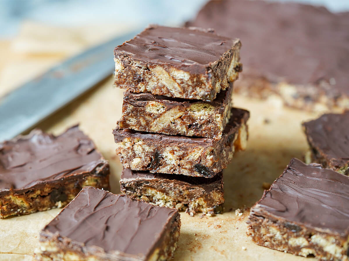 stack of four pieces of chocolate tiffin with knife and more blurred behind and to sides.