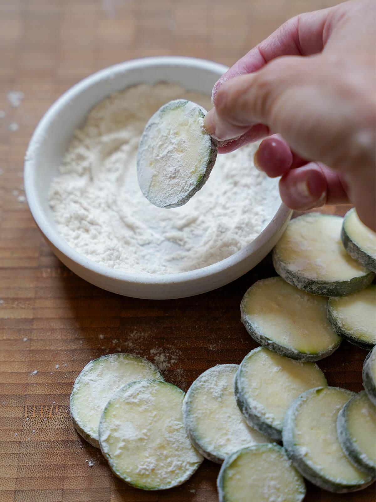 pidding a slice of zucchini in flour with other floured slices around dish.