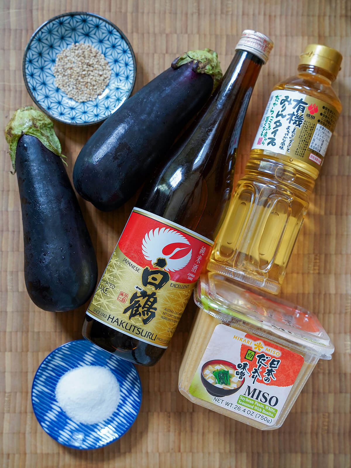 eggplants, sake bottle, box of miso, bottle of mirin and small dishes with sugar and sesame seeds.