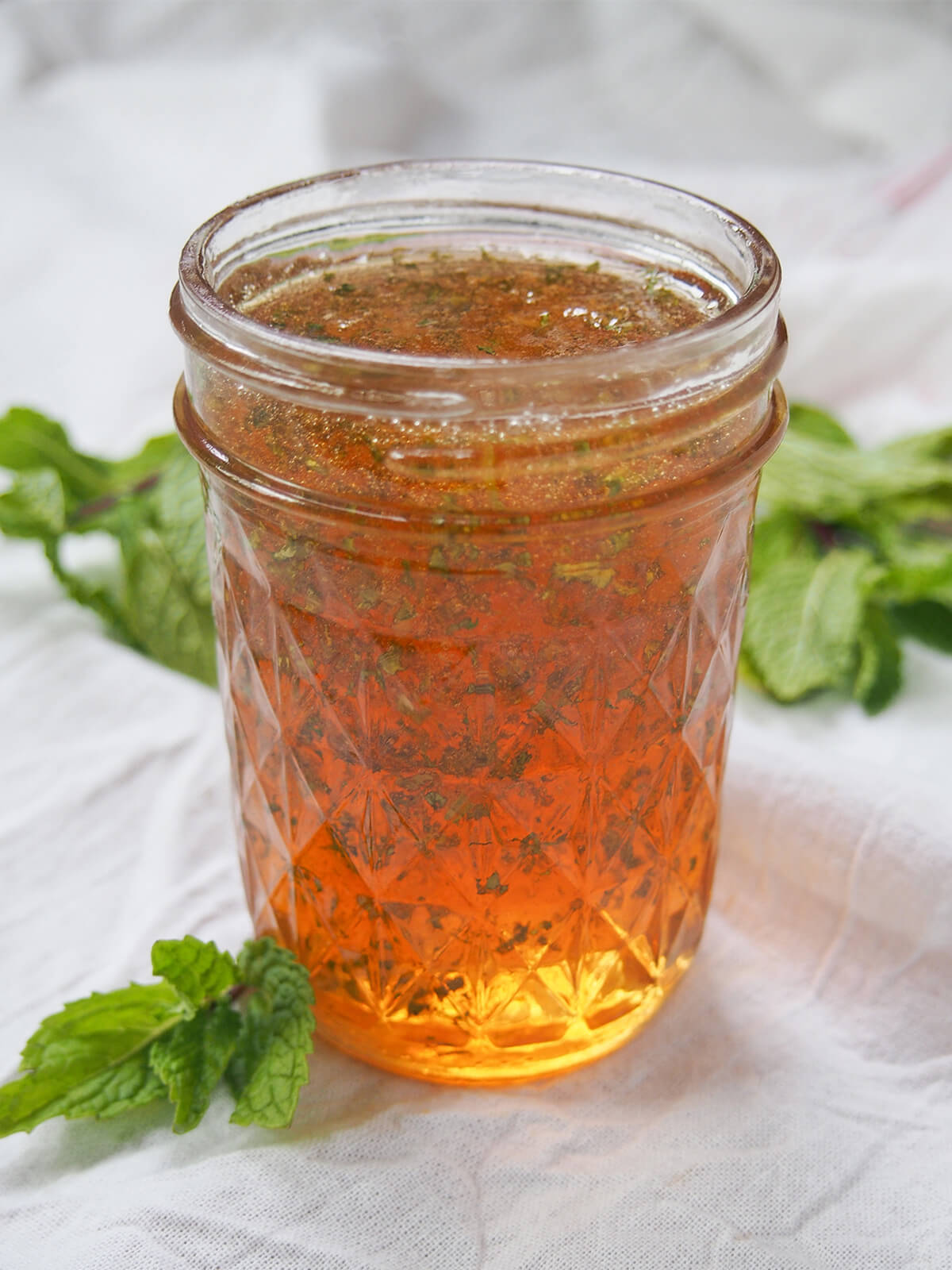 side view of jar or mint jelly with mint sprigs behind.