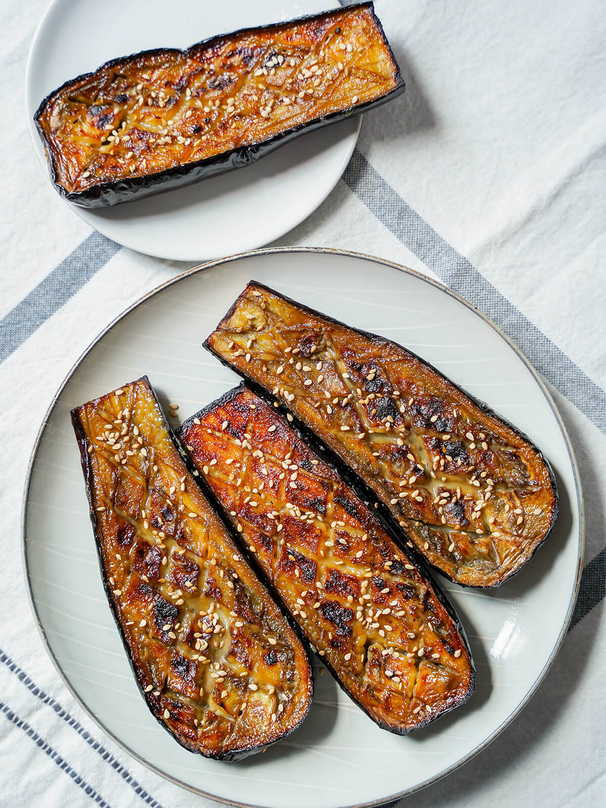 overhead view of three pieces of nasu dengaku, miso glazed eggplant, on a plate with another on small plate above.