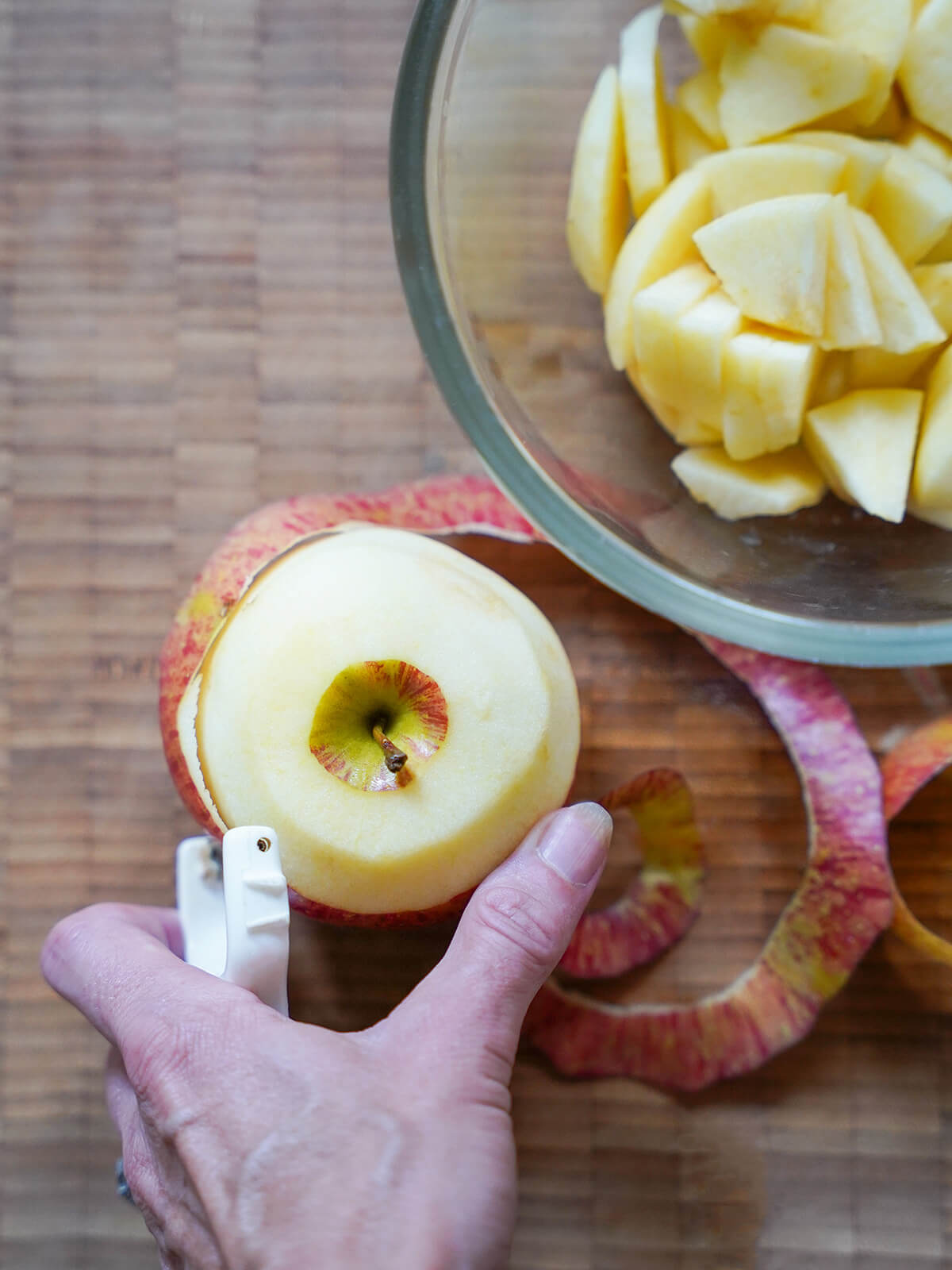 peeling apples for caramelized apples peeling an apple with a bowl of slices to one side.