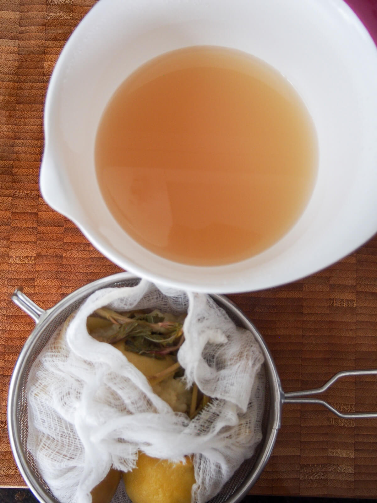 strained liquid in bowl with solids in cheesecloth in strainer below.