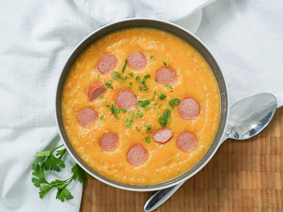 overhead view of a bowl of German potato soup, kartoffelsuppe, with spoon below and parsley stem to other side.