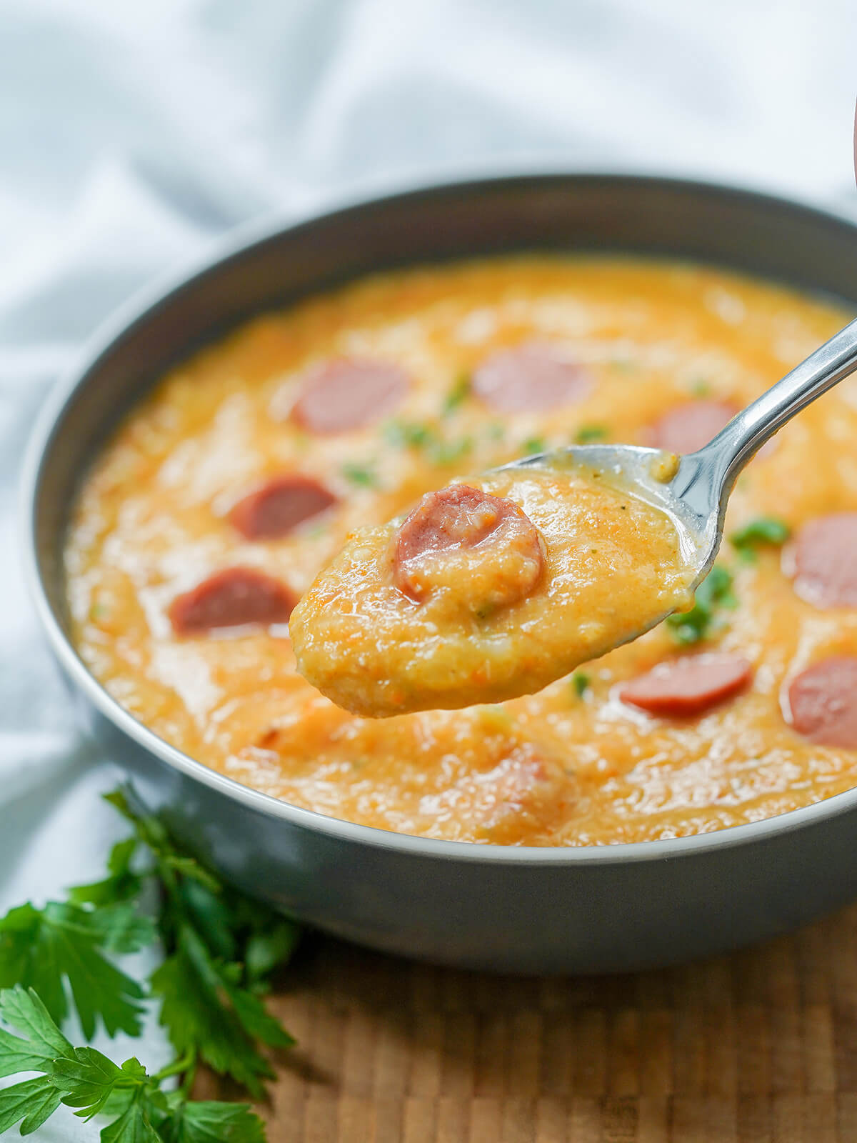 a spoon of German potato soup, Kartoffelsuppe, held above a bowl with sprig of parsley to side.