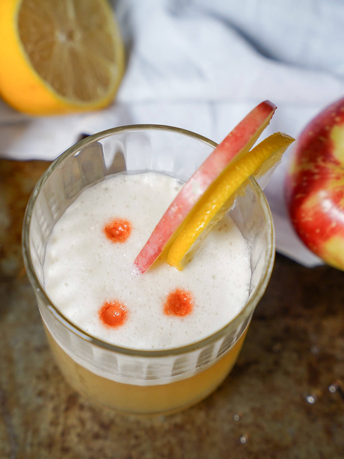 overhead view of glass of apple whiskey sour with drops of bitters on top.