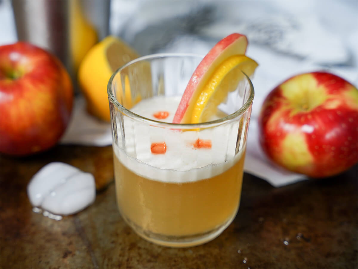 glass of apple whiskey sour with apples either side.