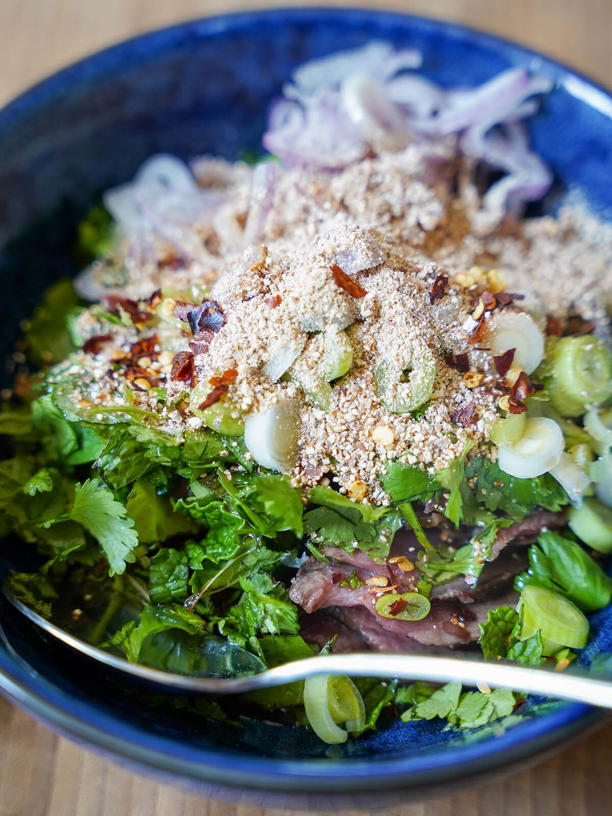 bowl showing herbs, ground rice, shallots and beef largely hidden at bottom.