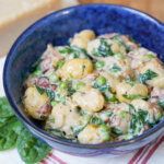 side view of bowl of creamy bacon gnocchi with spinach.