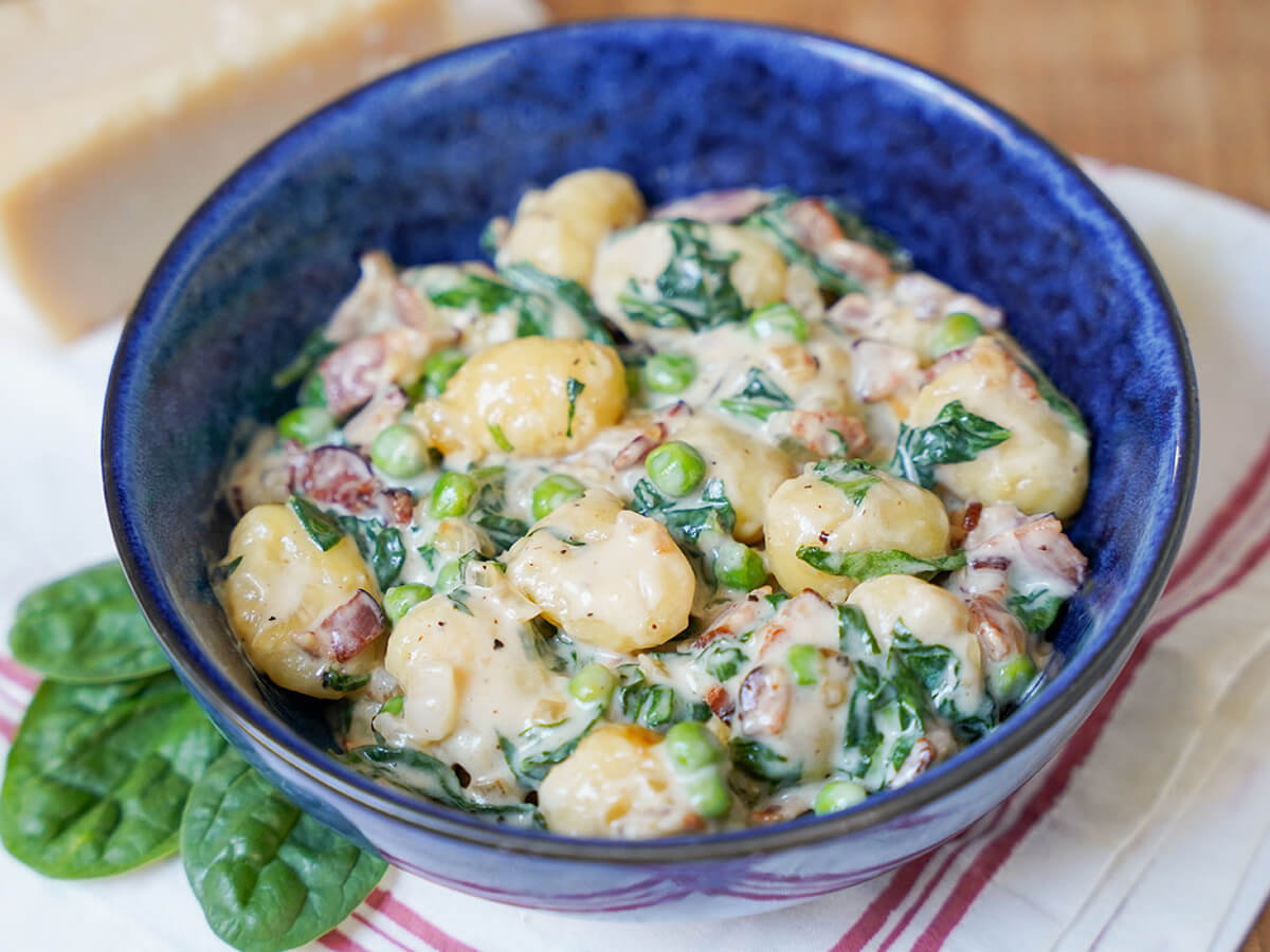 bowl of creamy bacon gnocchi with spinach with spinach leaves under bowl.