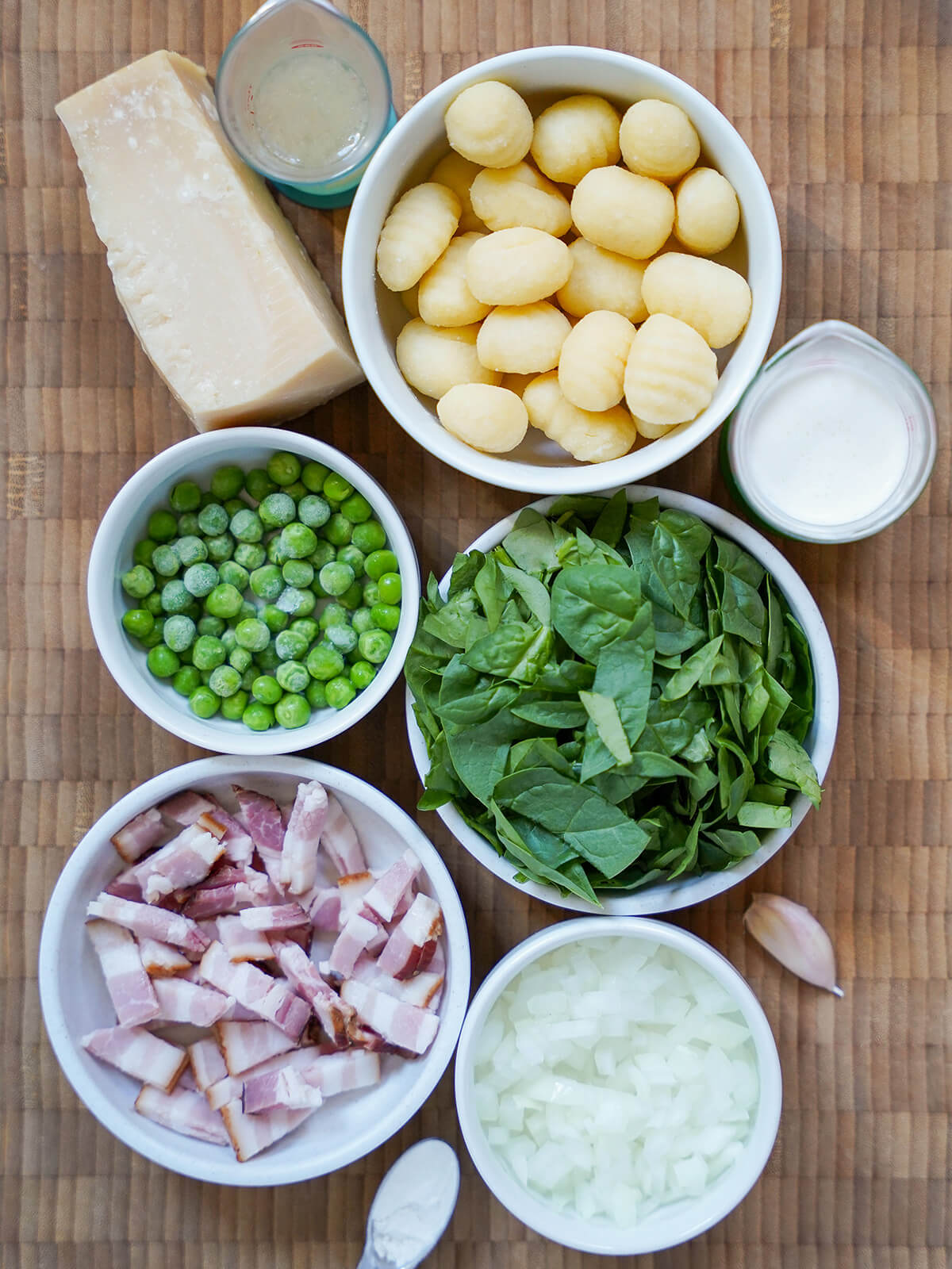 bowls with gnocchi, chopped spinach, peas, bacon, chopped onion with cheese, cream and stock around.