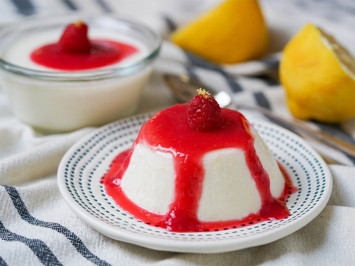 lemon panna cotta on plate with another in dish behind along with lemon halves.