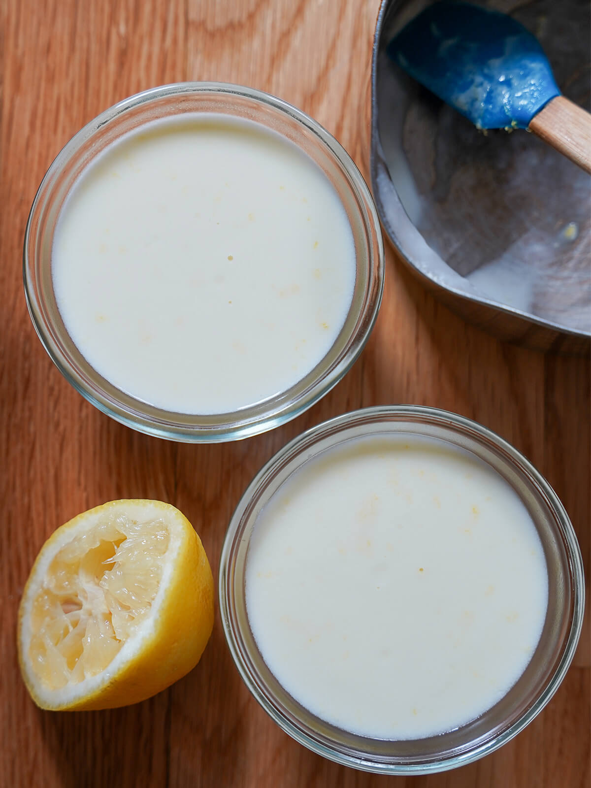 dishes of lemon panna cotta from overhead with squeezed lemon to side during making.