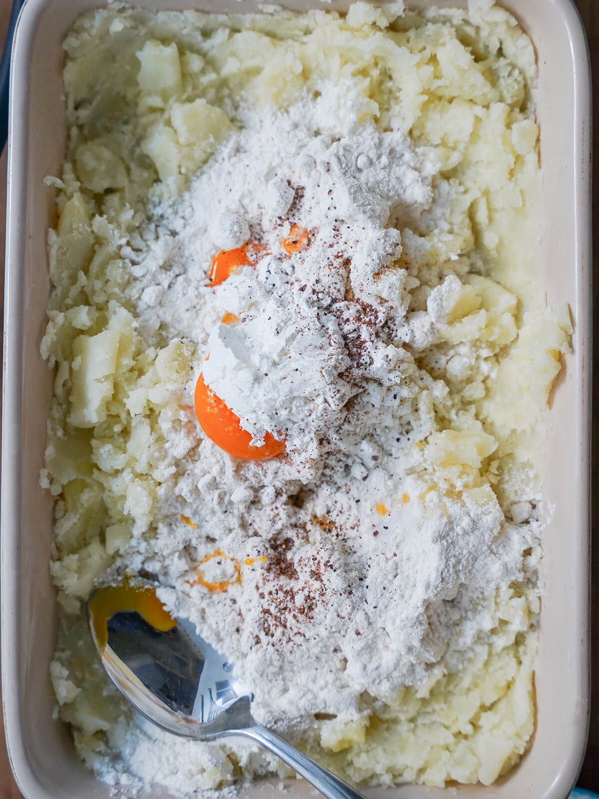 mashed potato in dish with egg yolk, flour and some seasoning on top.