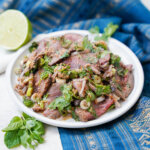 plate of nam tok waterfall beef salad with herbs to front of plate.