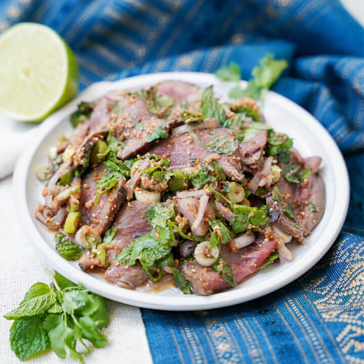 plate of nam tok waterfall beef salad with herbs to front of plate.