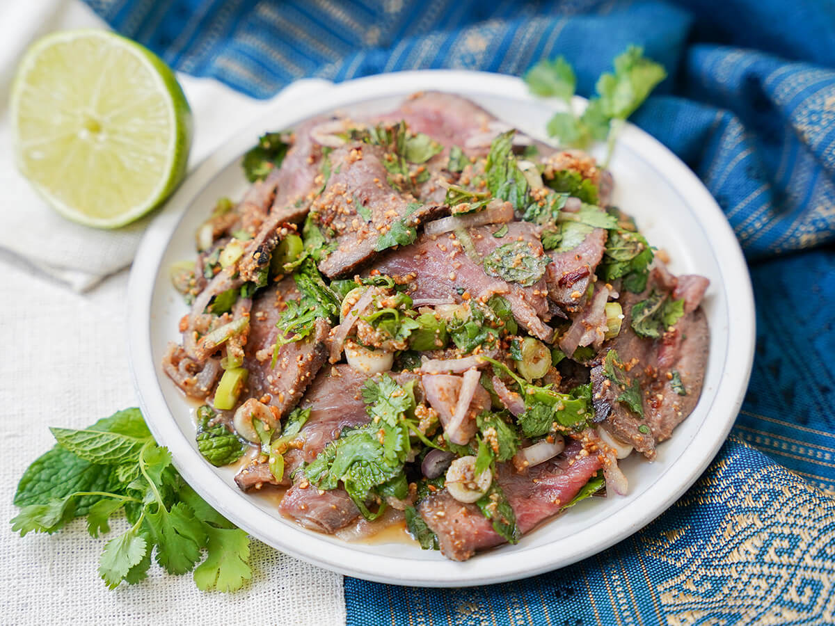 plate of nam tok waterfall beef with half lime and herbs to one side.