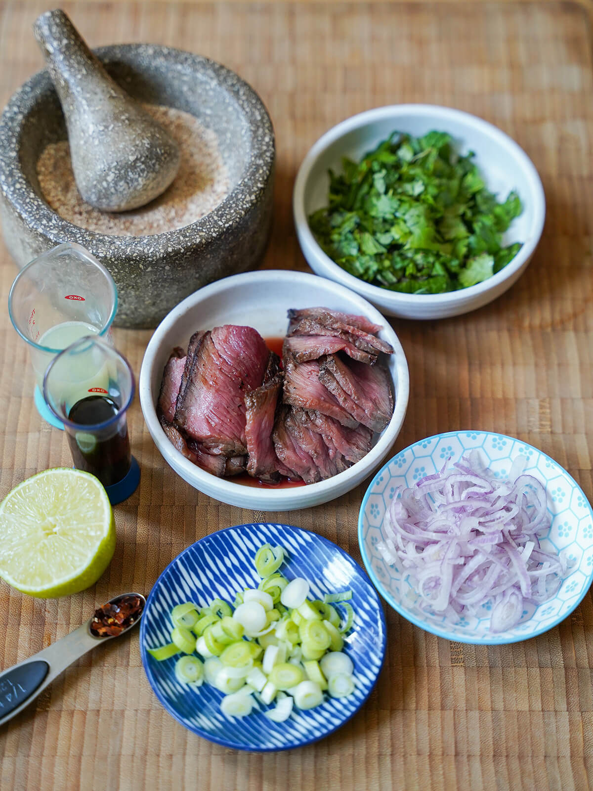 plates of chopped herbs, sliced shallots and green onions, sliced beef with mortar of ground rice.