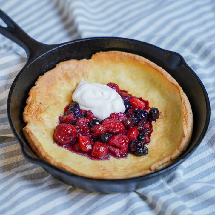 Individual Dutch baby pancake topped with berries and some yogurt on top.
