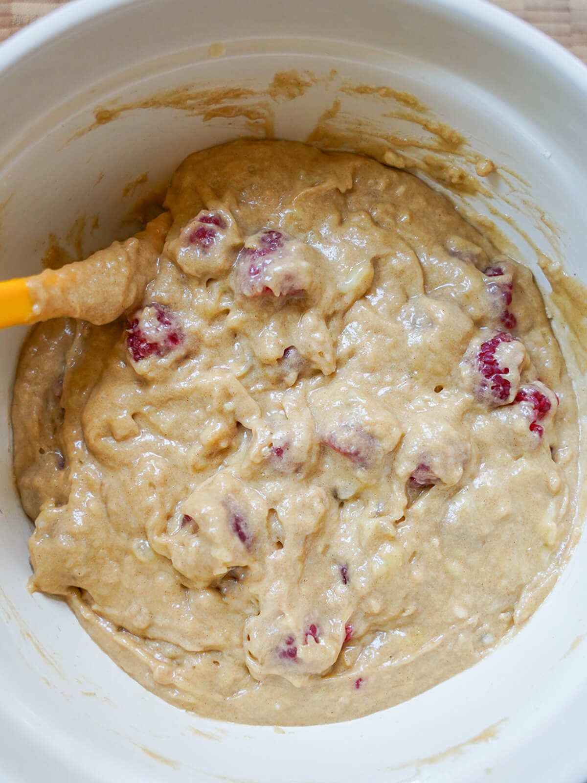 batter with raspberries folded into it in bowl with spatula to one side