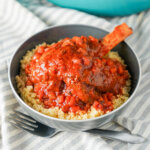 Braised lamb shank in bowl with couscous under and sauce over.