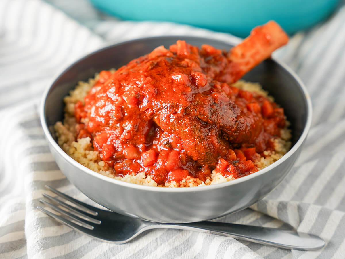 Braised lamb shank in bowl with sauce over top and fork in front of bowl.