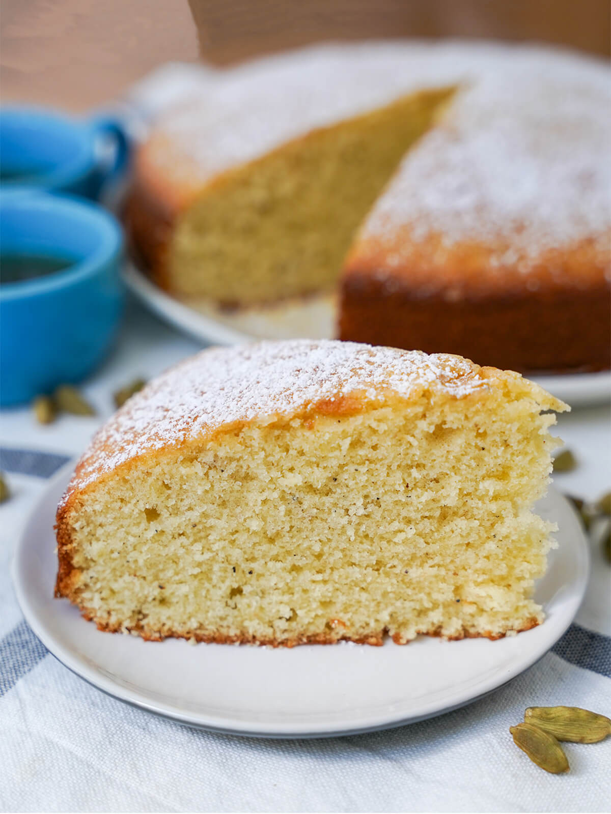 slice of cardamom cake on a small plate with blurred rest of cake in background.
