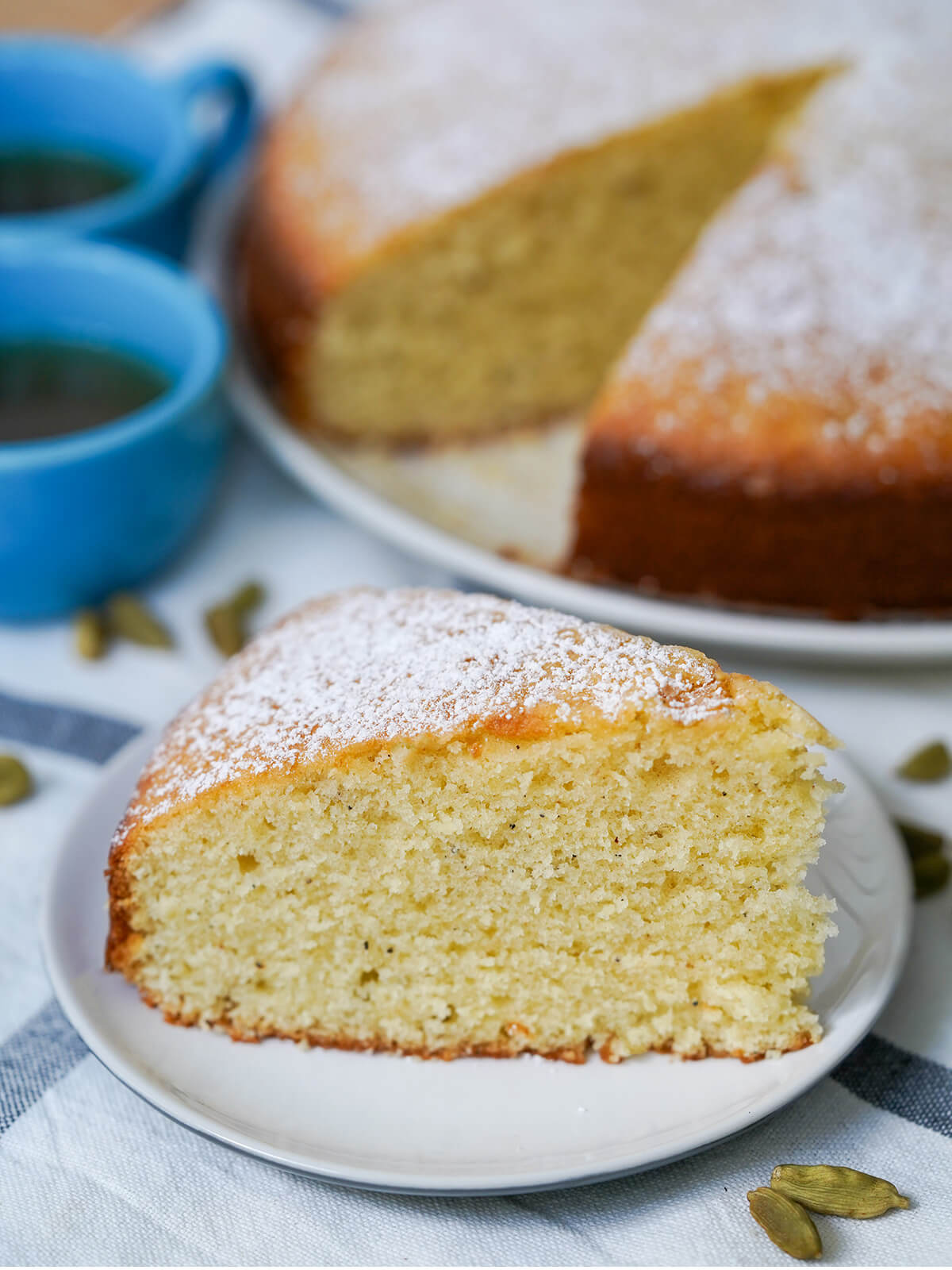 slice of cardamom cake on plate in front of rest of cake.