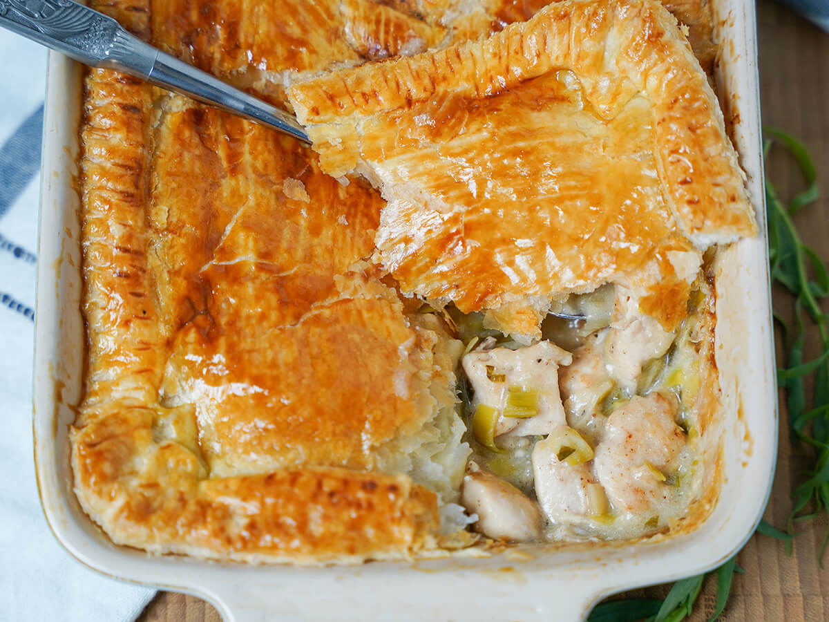 end of dish of chicken and leek pie with tarragon with part of pastry lifted up to show chicken filling below.