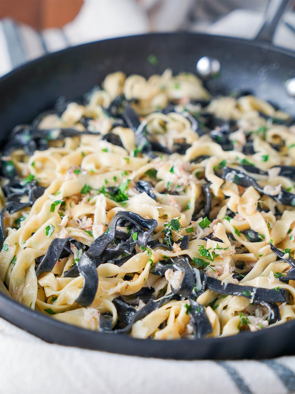 skillet of black and regular pasta with crab and parsley through it.