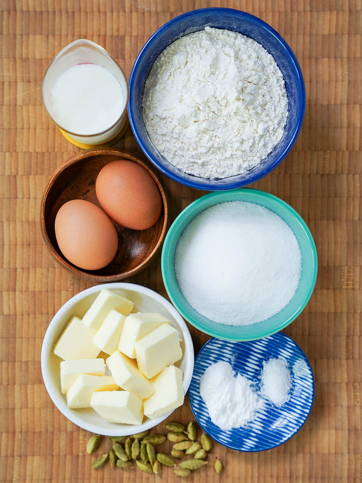 bowls of sugar, flour, butter, eggs, measure of milk and cardamom pods below.