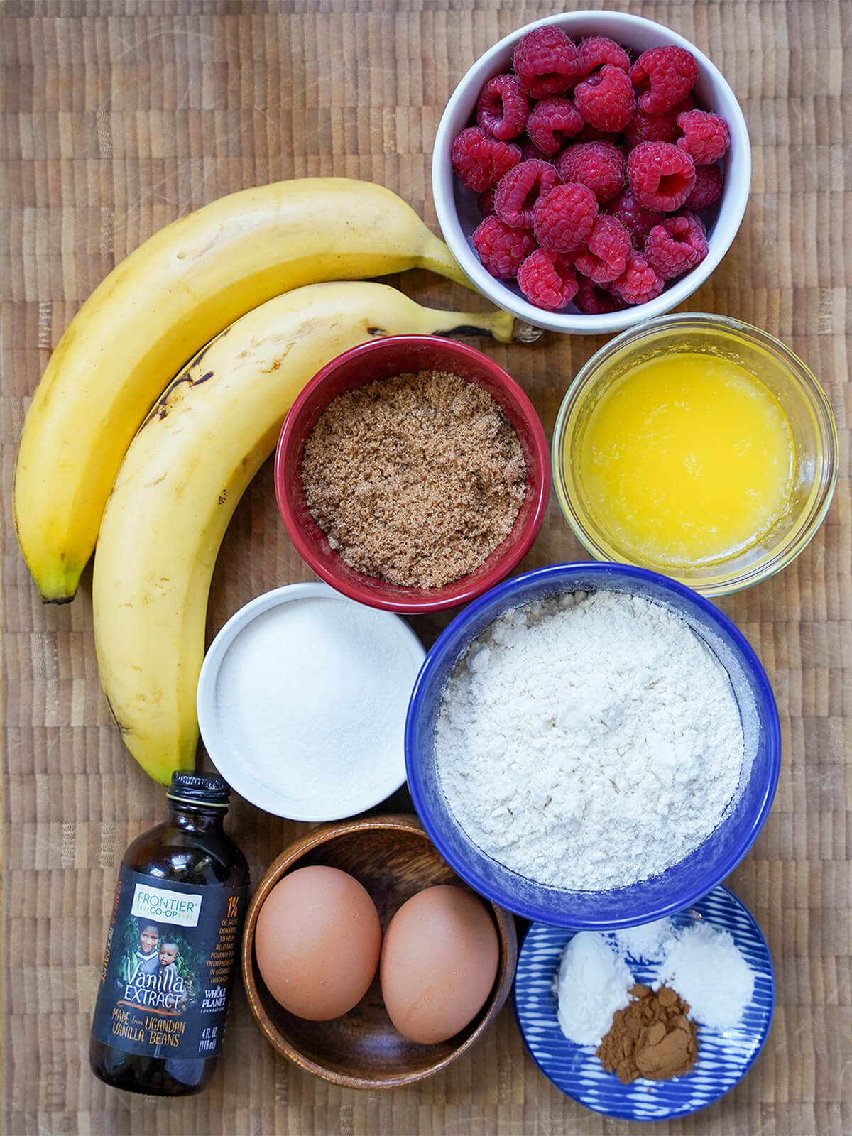 bananas, bowls of raspberries, sugar, melted butter, flour, eggs and spices.