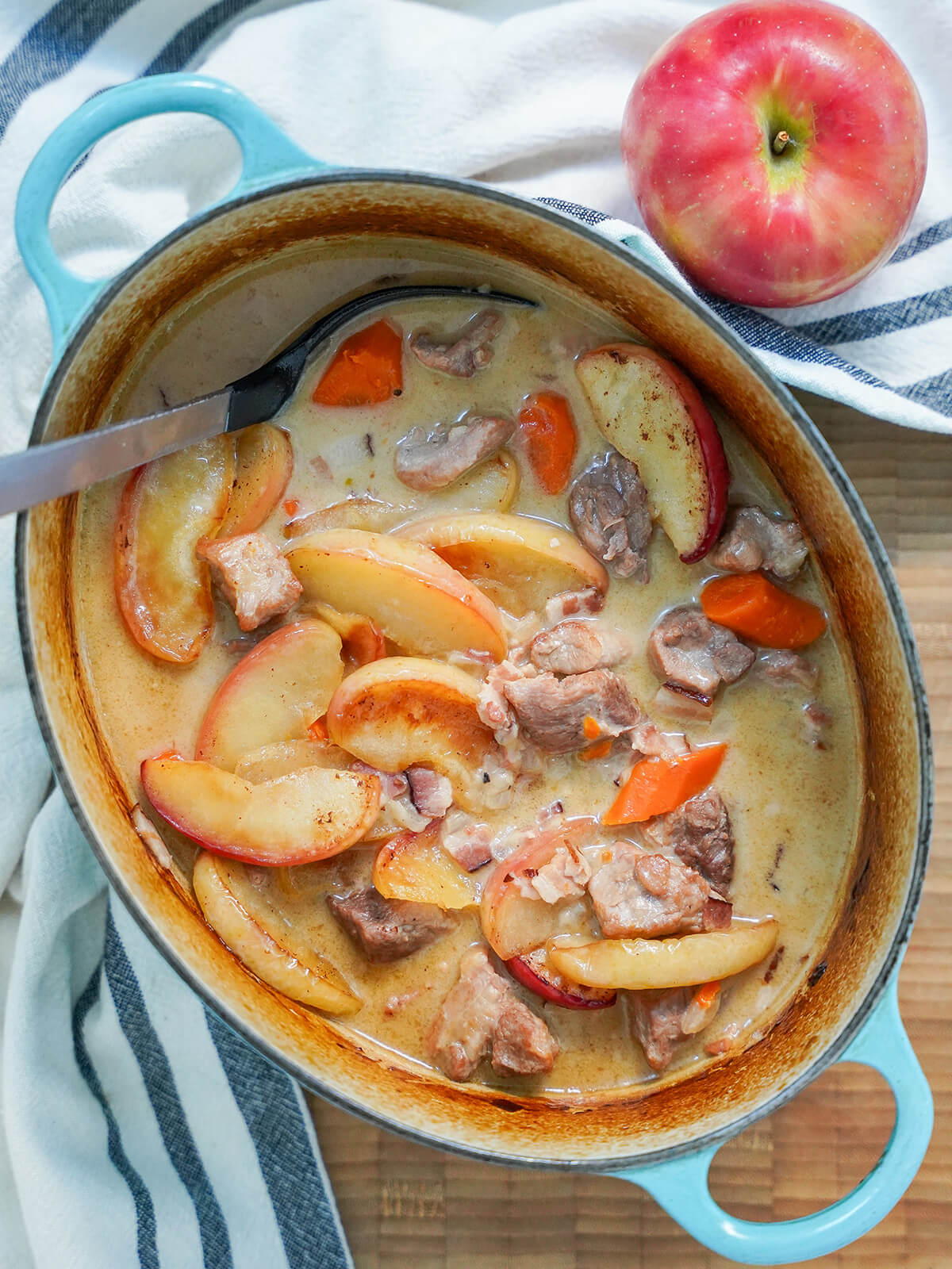 overhead view of pot of pork and cider casserole with apple above pot.