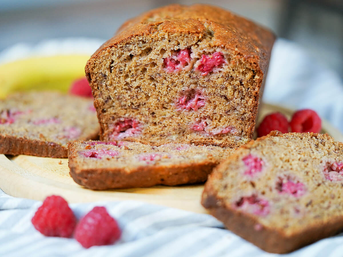 side on raspberry banana bread with slices either side and raspberries to side.