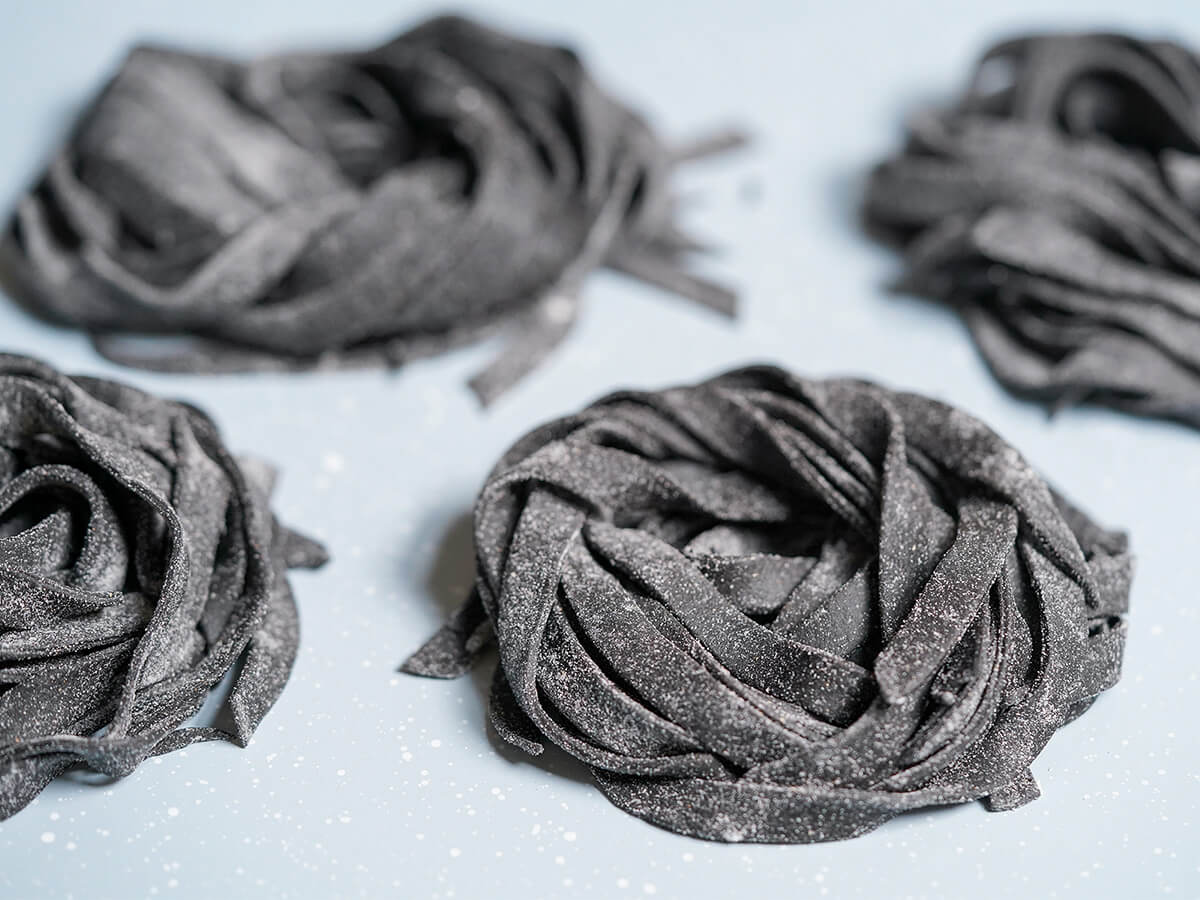 stacks of floured squid ink pasta on tray.