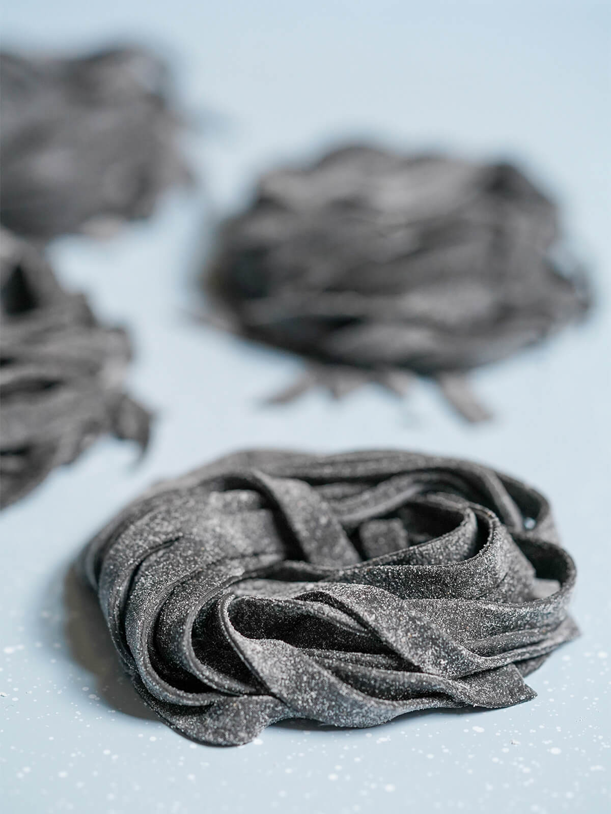 close view of a stack of squid ink pasta with more blurred behind.