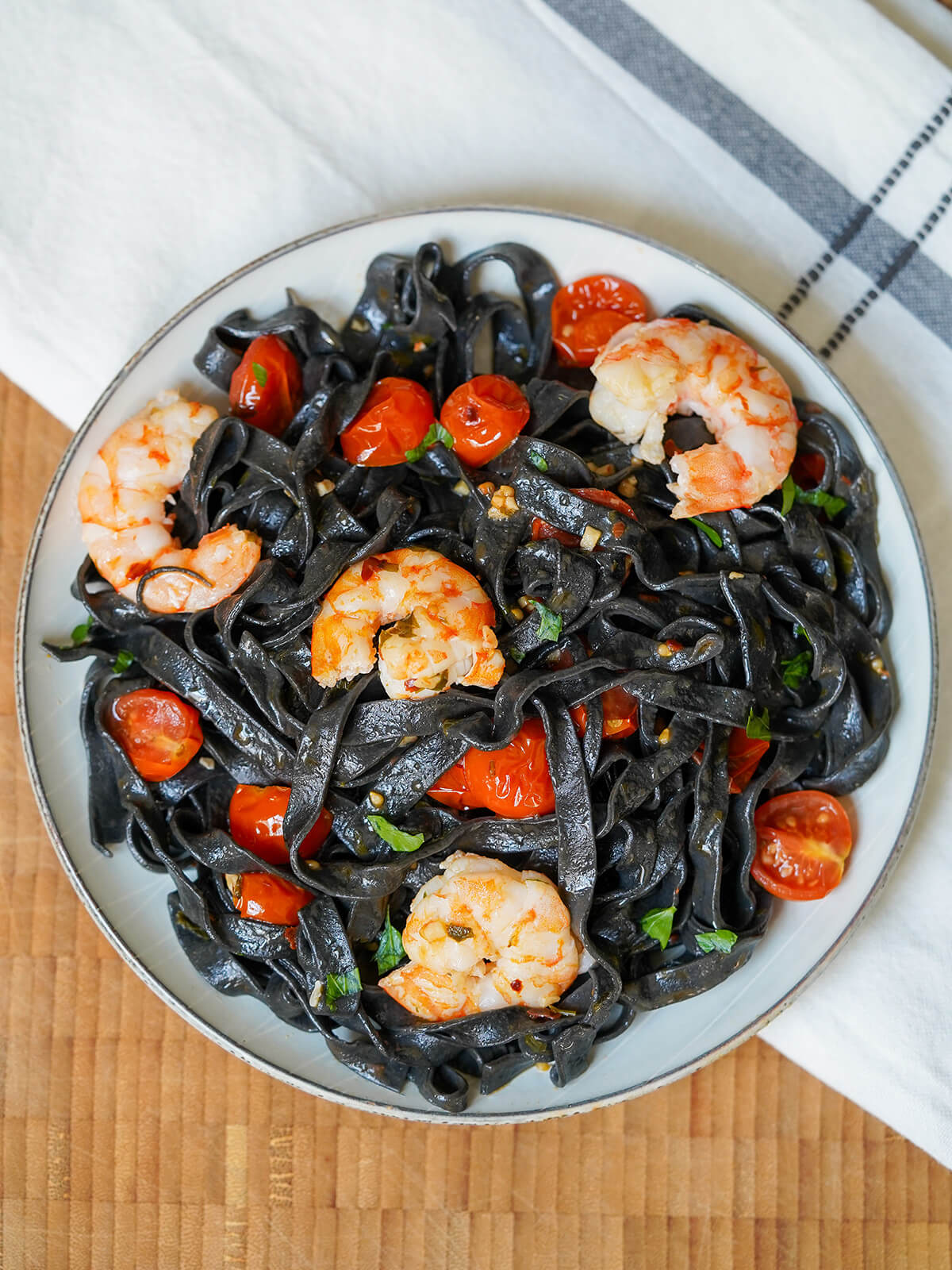 overhead view of a plate of squid ink pasta with shrimp and tomato.