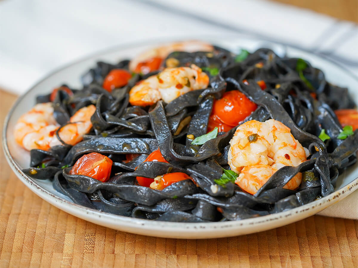 side view of plate of squid ink pasta with shrimp and tomato.