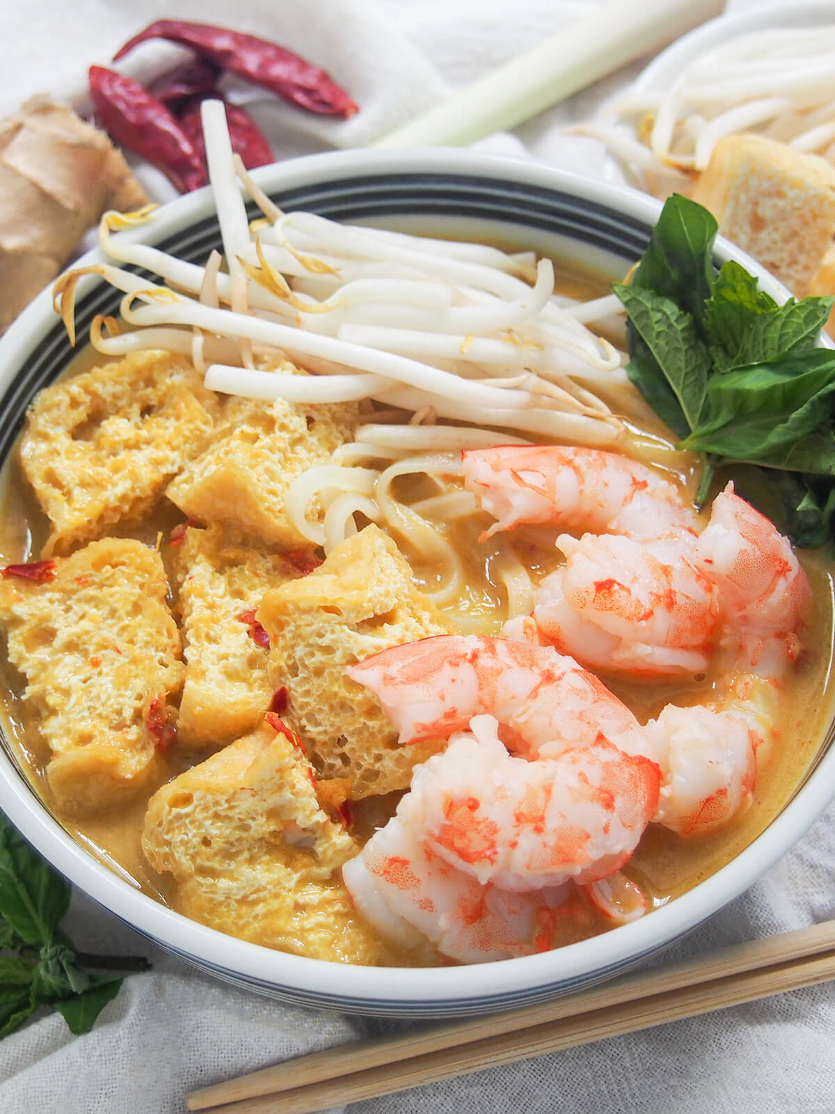 close view of bowl of Singapore laksa topped with shrimp and tofu puffs.